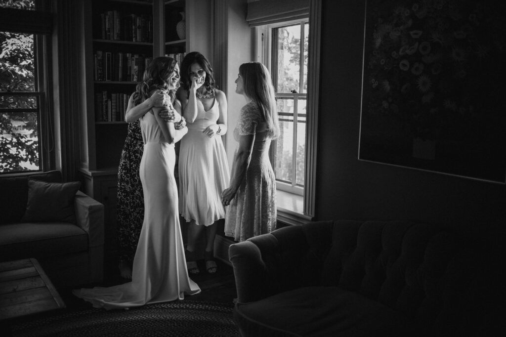 Three women sharing a moment in a room with bookshelves and elegant decor at a Stonover Farm Wedding.