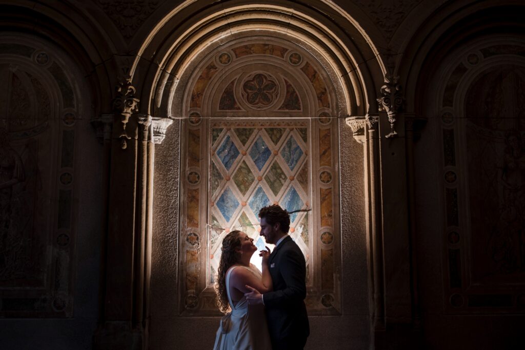 Couple embracing in a warmly lit archway during their Central Park wedding photos.