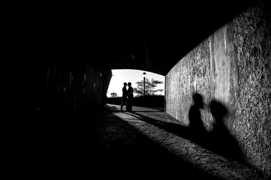Silhouettes of two people standing under a bridge in Fort Tryon Park with their shadows cast on the ground.