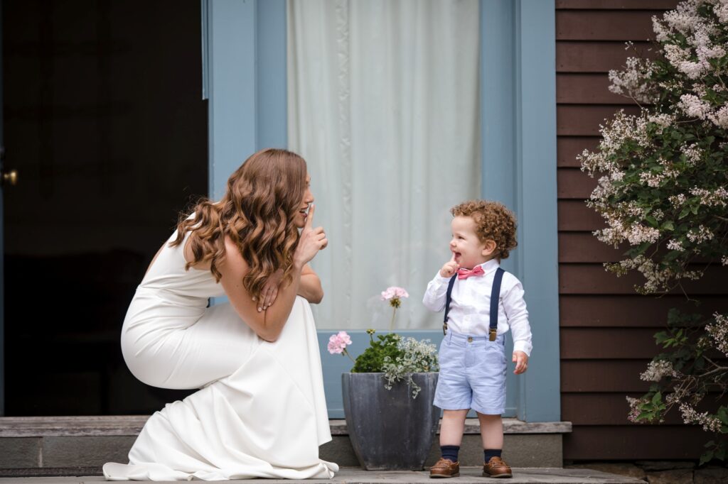 A woman and a young child engage in a playful conversation outdoors near a blooming shrub at a Stonover Farm Wedding.