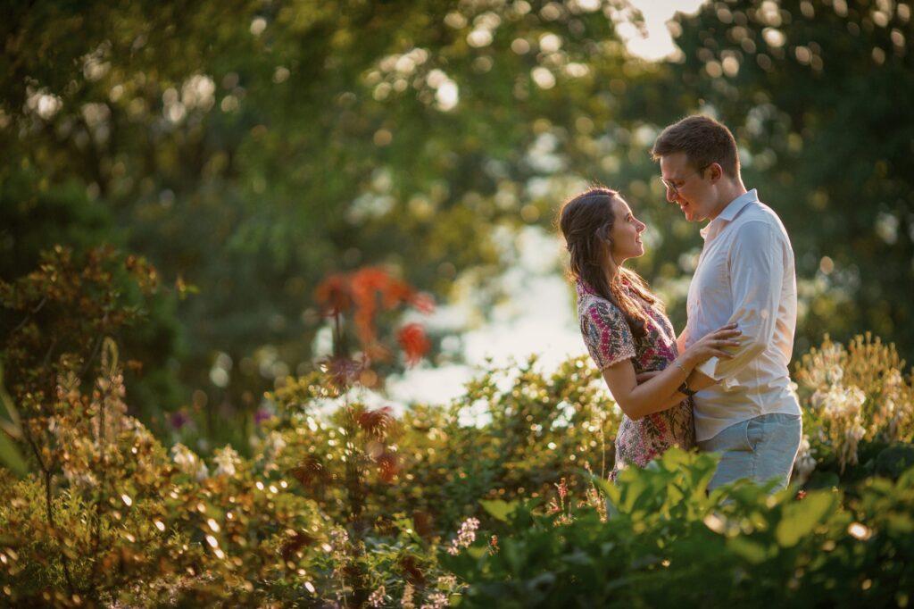 A couple sharing a tender moment amidst sunlit greenery during their Fort Tryon Park engagement photos.