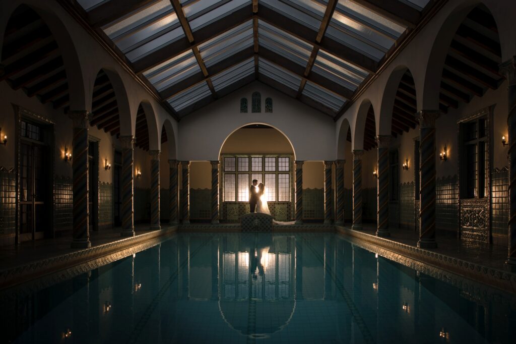 An indoor pool at Pleasantdale Chateau in a luxurious setting with arched doorways and a person standing at the far end, silhouetted against a glowing window.