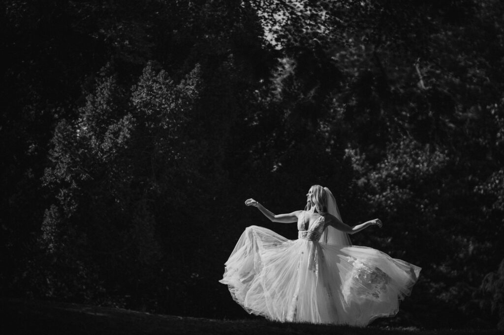 A woman in a white gown twirling in a shaded forest clearing during her Bronx Zoo Stone Mill wedding.