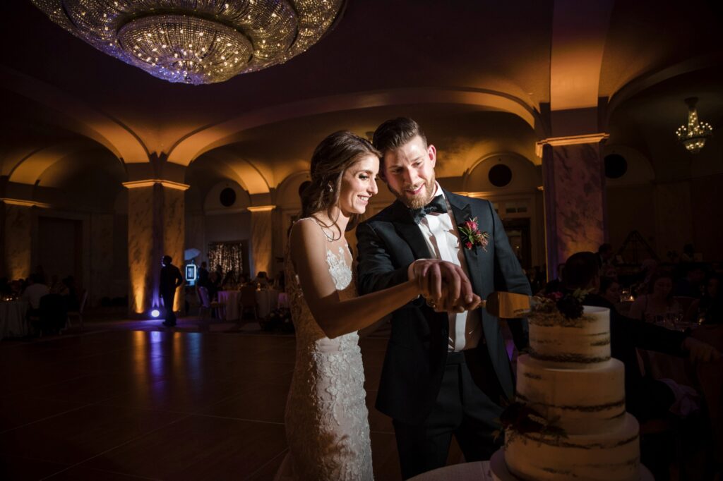 A bride and groom cutting their wedding cake under elegant chandelier lighting at the Ritz Carlton Philadelphia.
