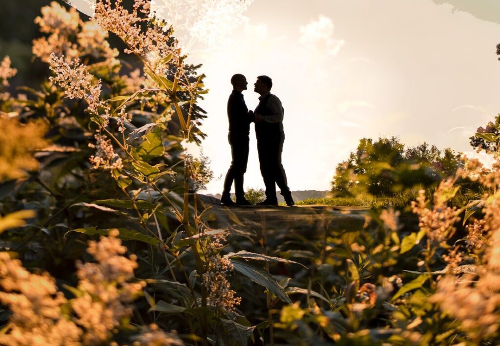 Two people standing under a tree at sunset in Fort Tryon Park, silhouetted against a warm, backlit natural setting for their engagement photos.