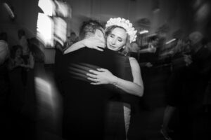 A monochrome photo of a woman wearing a floral headpiece dancing closely with a man at a Bourne Mansion wedding, captured with motion blur.