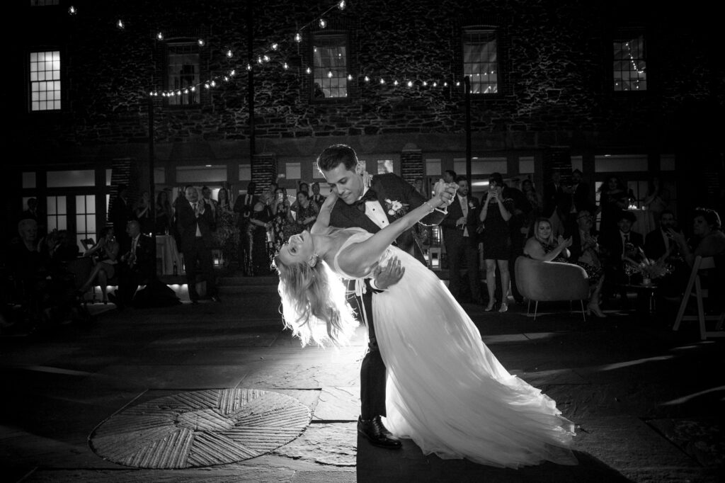 A couple sharing a dramatic first dance dip at an outdoor Bronx Zoo Stone Mill wedding with onlookers in the background.