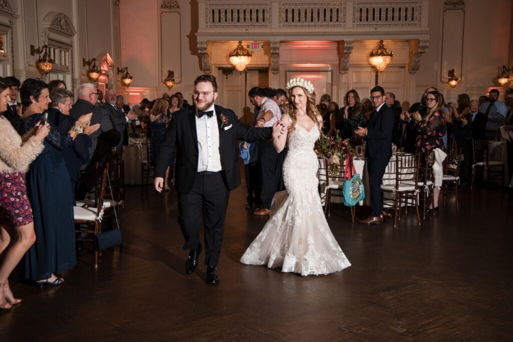 Newlywed couple walking through a crowd of guests at their Bourne Mansion wedding.
