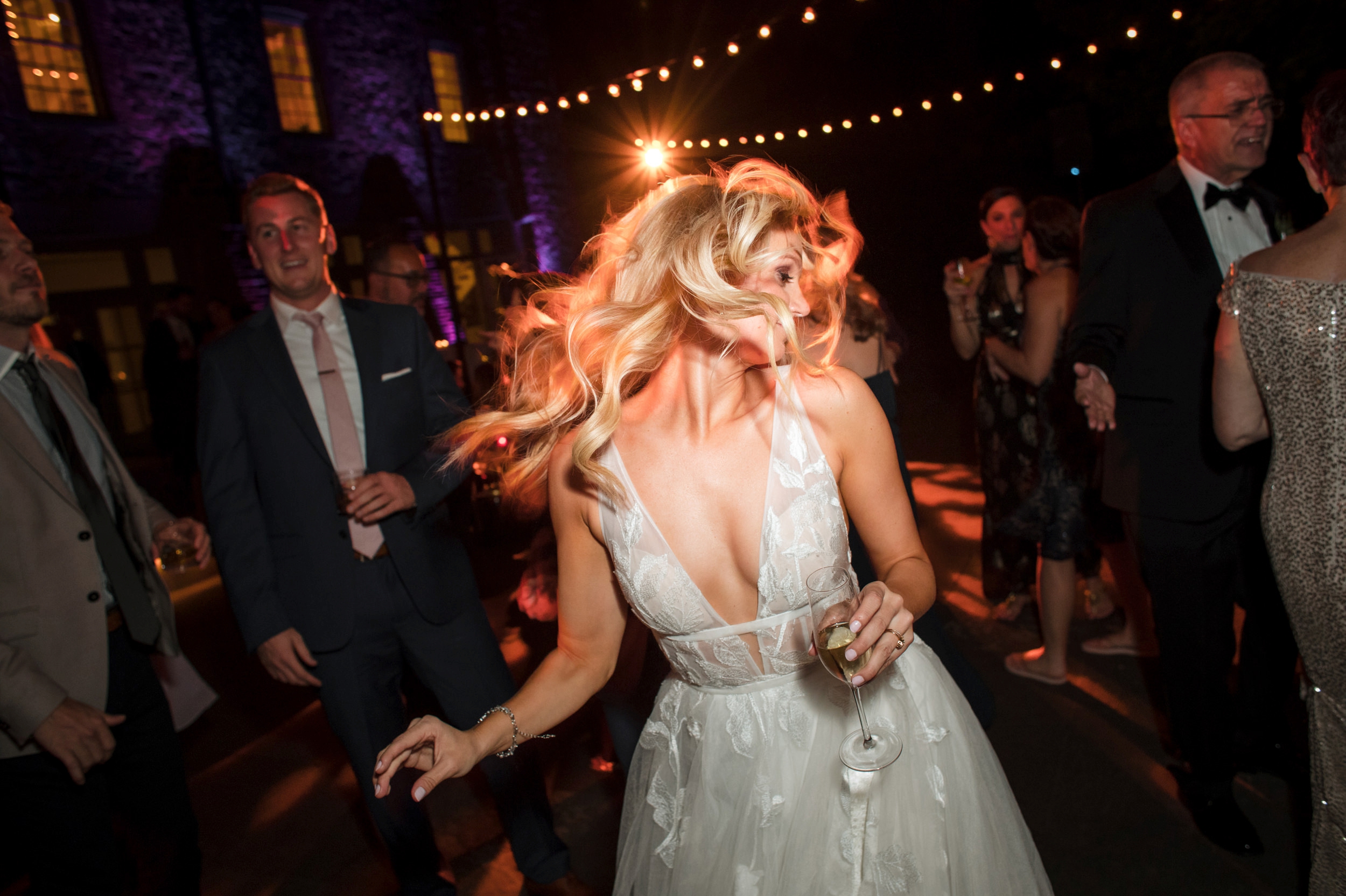 A woman in a white dress dancing at a Bronx Zoo Stone Mill wedding with string lights and guests in the background.