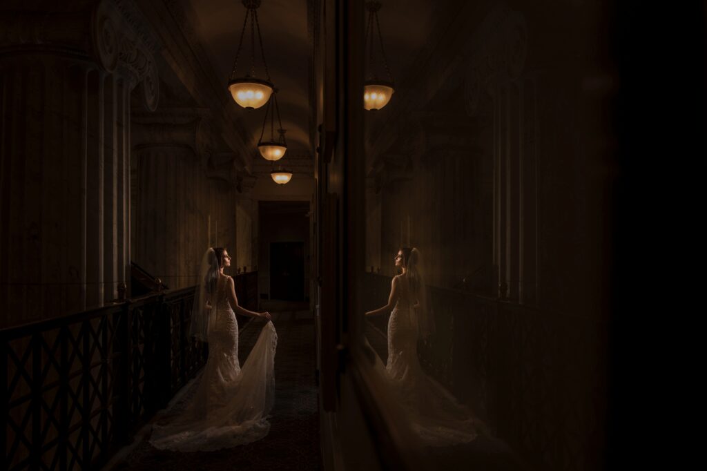 Bride in a dimly lit vintage hallway at the Ritz Carlton Philadelphia, with a reflective mirror image to her side.