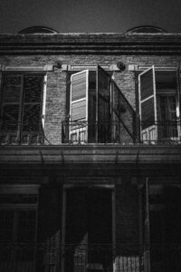 A historic black-and-white New Orleans brick building with open wooden shutters