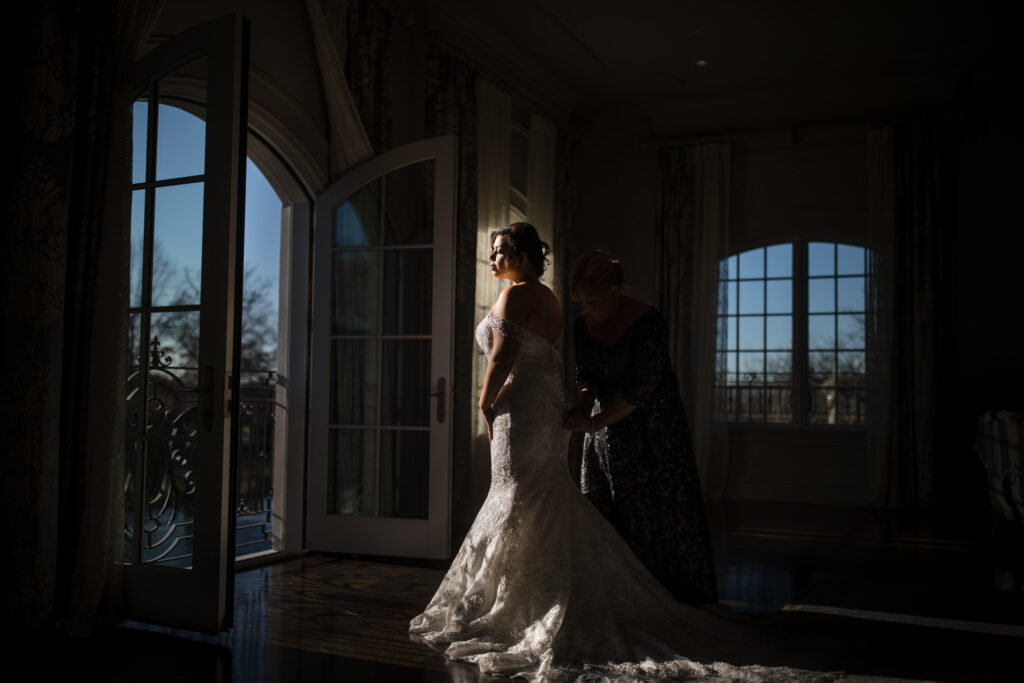 A bride being assisted with her dress in a dimly lit room before a Park Chateau wedding ceremony.