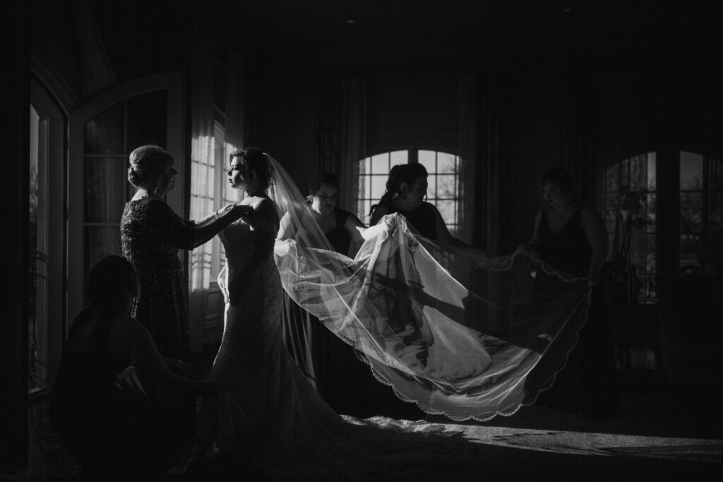 Bridesmaids arranging the bride's veil in a dimly lit room at a Park Chateau wedding.