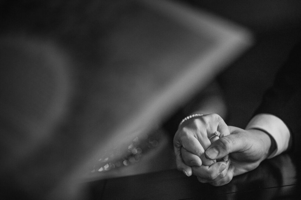 Close-up of a person's hands gently clasping another's at a Crystal Tea Room Philly wedding, wearing a wedding ring, with a blurred laptop in the background.