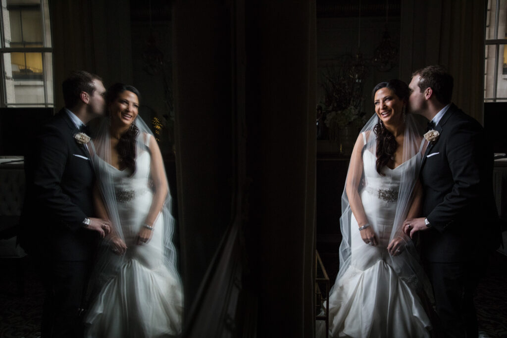 A bride and groom laughing together, reflected in a mirror in a dimly lit Crystal Tea Room during their Philly wedding.