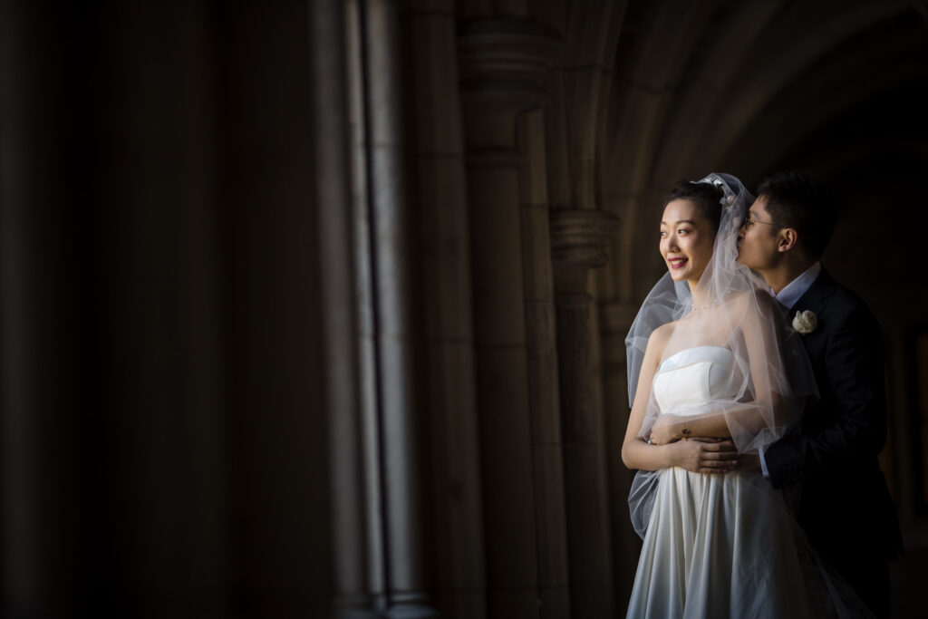 A bride and groom standing close together under an arched doorway at Princeton University, bathed in soft light.