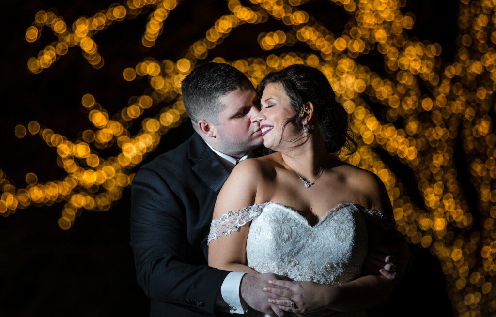 Newlyweds embrace at night with twinkling lights in the background at their Park Chateau wedding.