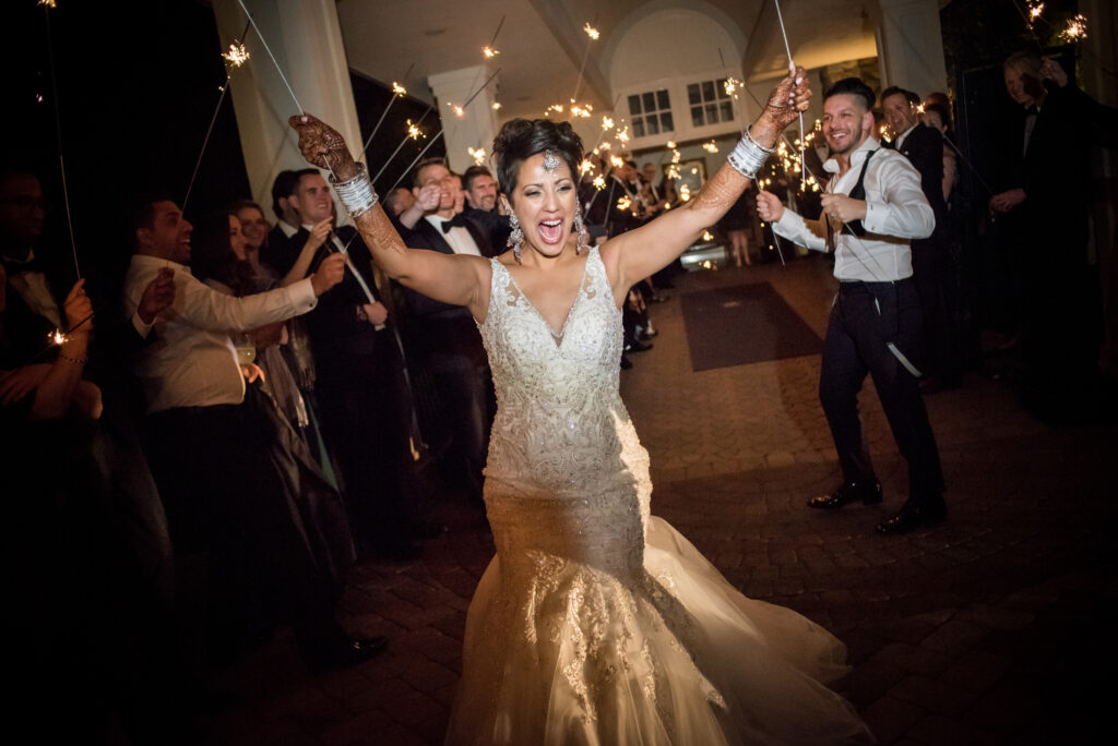 A joyful bride running with sparklers at a Crystal Plaza wedding, surrounded by cheering guests at night.
