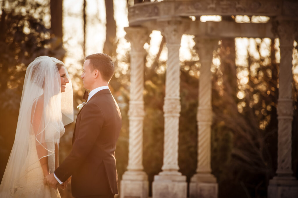 A bride and groom standing close together near ornate columns at a Crystal Plaza wedding, bathed in golden sunset light.