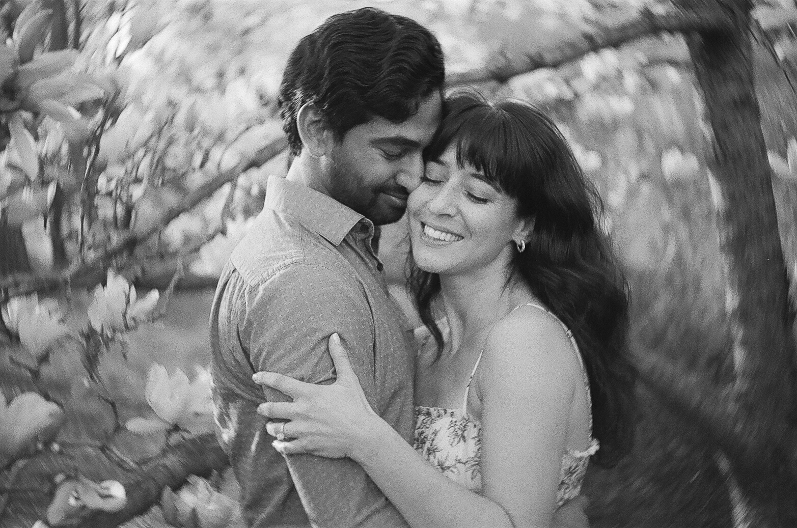 A monochrome film image of a smiling couple embracing tenderly among blooming flowers.