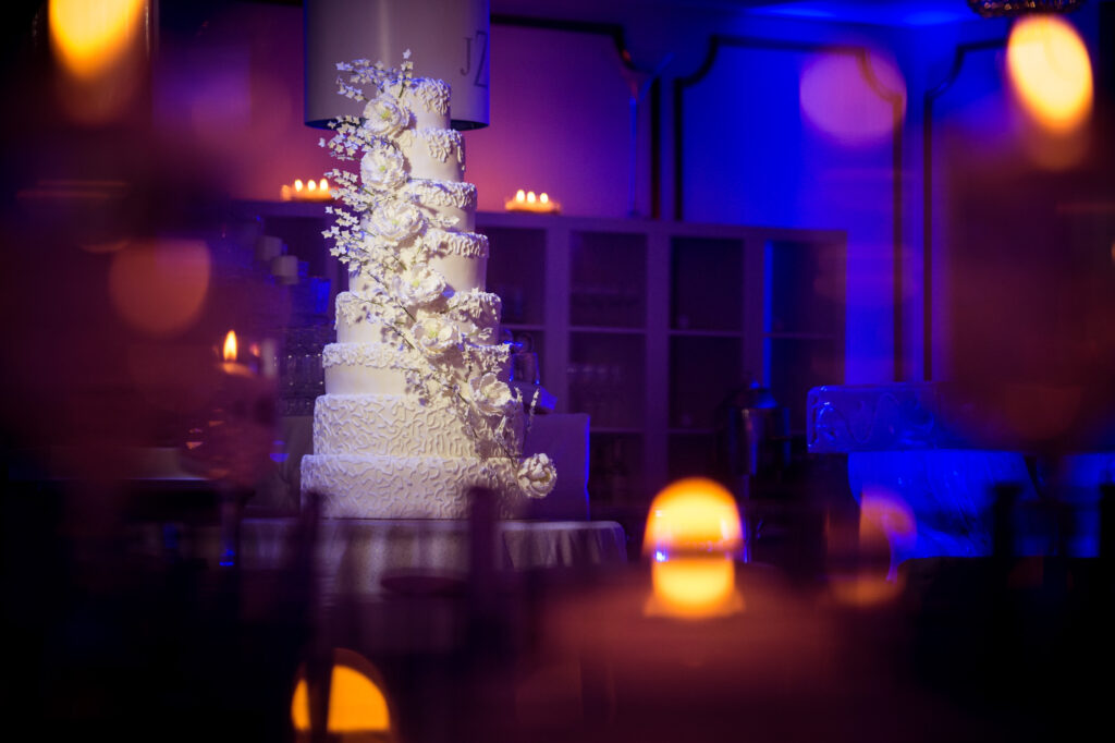 Elegant multi-tiered wedding cake adorned with white flowers, displayed at Crystal Plaza in a dimly lit room with glowing candles in the foreground.