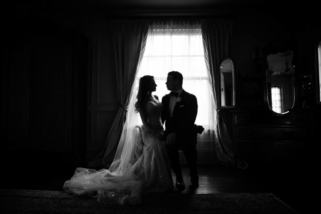 A silhouette of a bride and groom holding hands at a Park Savoy wedding, illuminated by light from a window in a dimly lit room.