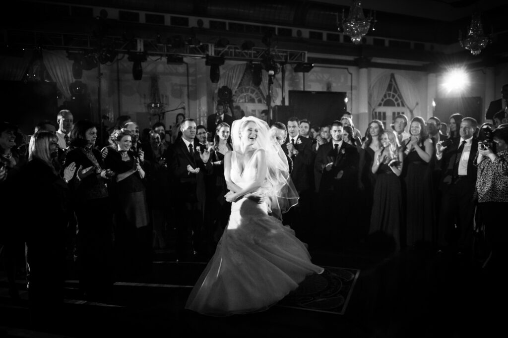A bride joyfully dancing in a ballroom at a Crystal Plaza wedding, surrounded by applauding guests at the reception.