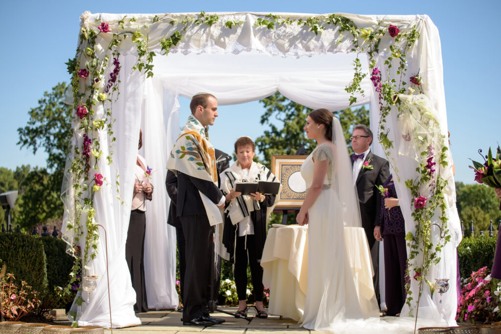 A Park Savoy wedding ceremony outdoors under a floral arch with a bride and groom facing an officiant, while a best man watches.