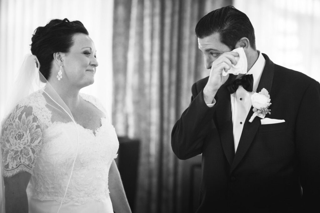 In a heartfelt black and white photo, a bride and groom share a touching moment as the groom wipes away a tear.