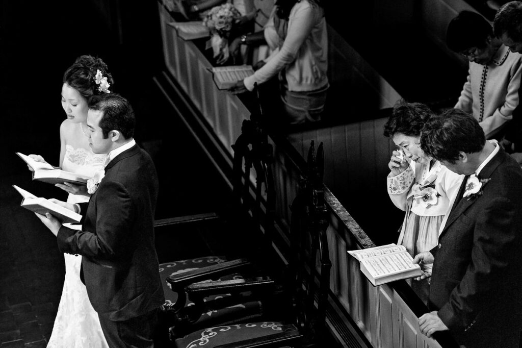 A bird's-eye view of a wedding couple reading together in a church, as an emotional family member wipes away tears on the sidelines.