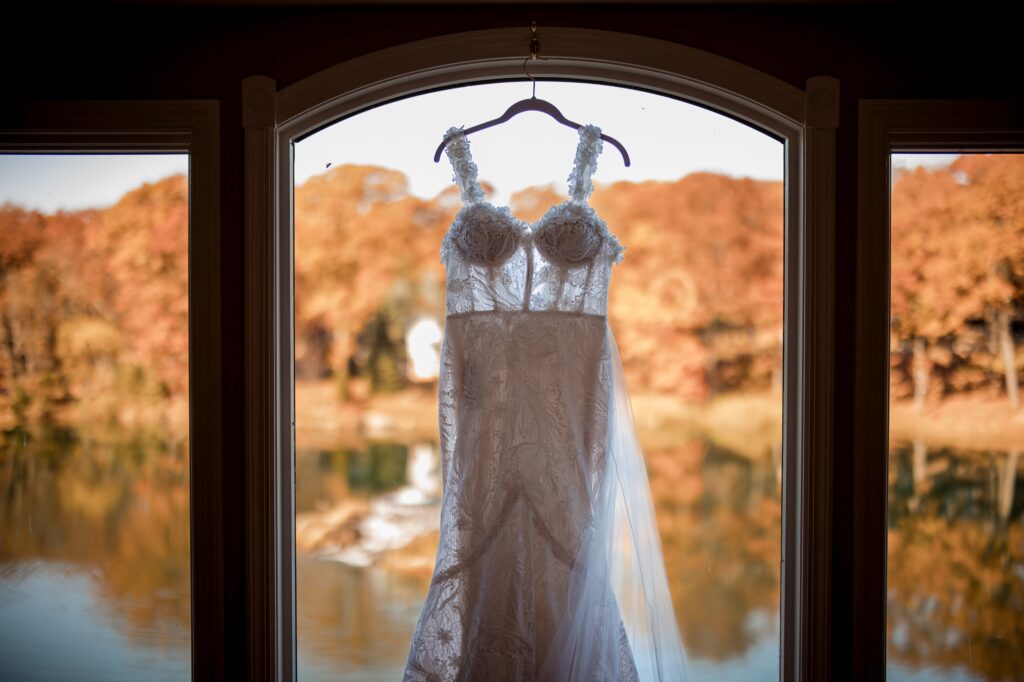 A wedding dress hanging in a window frame at Rock Island Lake Club, with a scenic autumn lake and trees in the background.