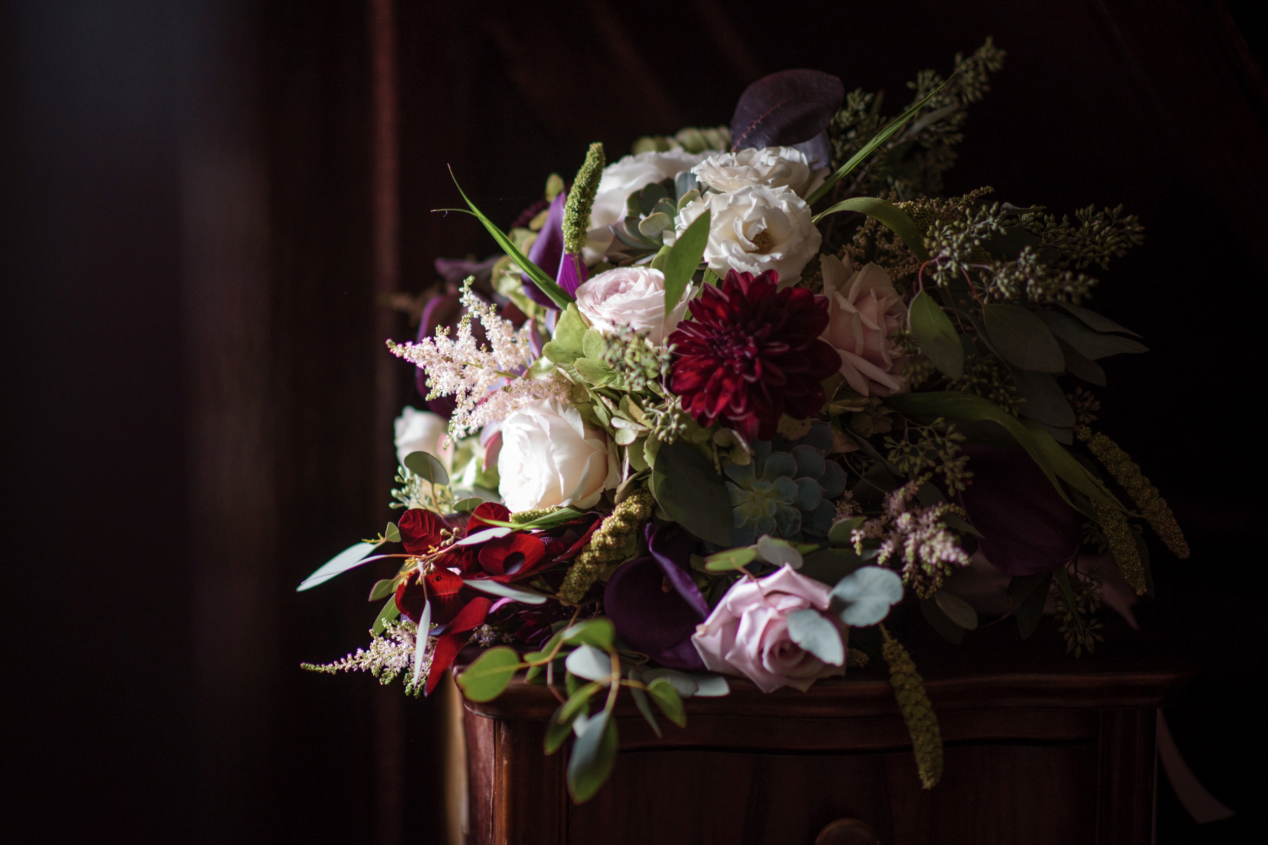 A bouquet of flowers with roses and dahlias on a wooden surface at Hotel du Village, highlighted by soft natural light.