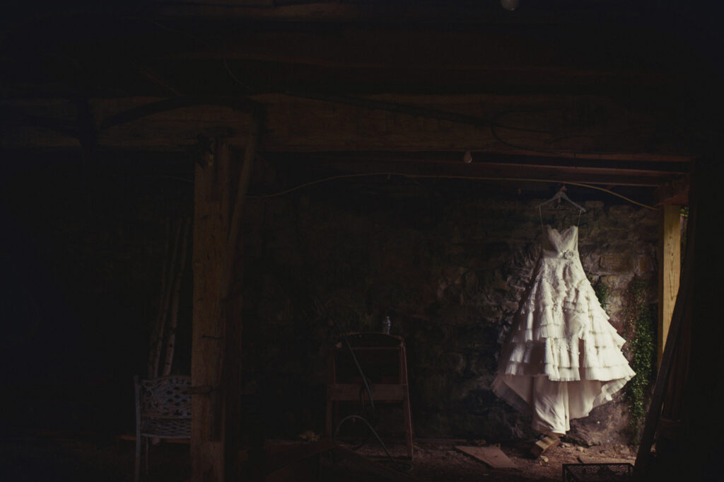 A wedding dress hanging in a dimly lit, rustic basement with stone walls and wooden beams at the Crossed Keys Inn in Andover.