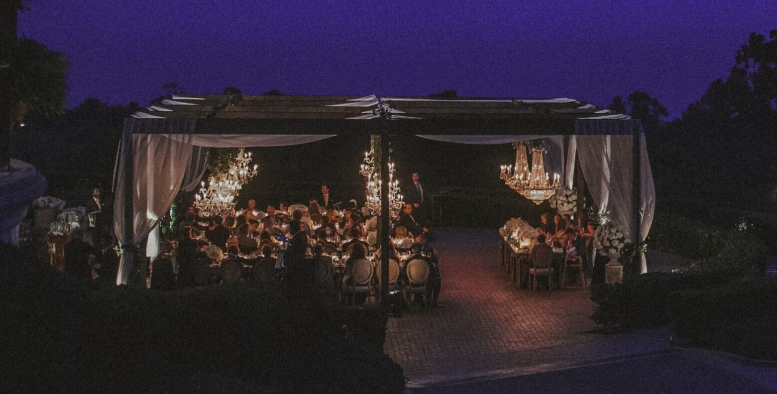 Nighttime wedding reception outdoors at Resort at Pelican Hill with an illuminated gazebo, elegantly setup tables, and a vibrant purple sky.