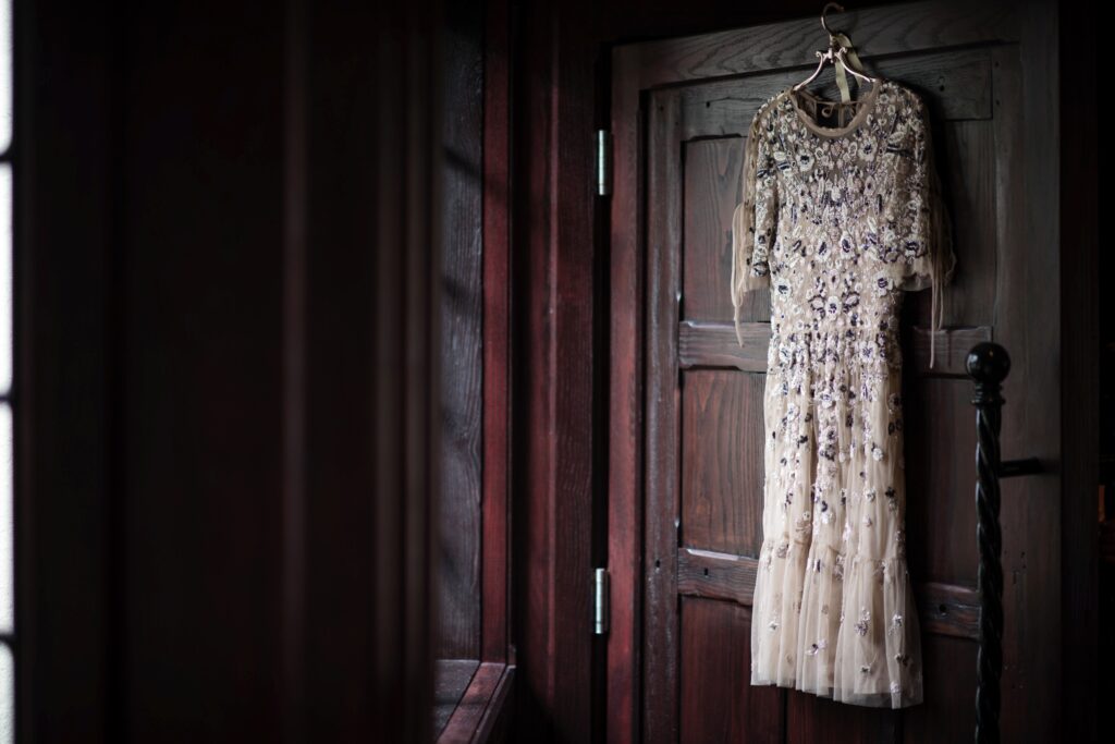 An intricately embellished dress hanging on a wooden door in a dimly lit room at Hotel du Village.