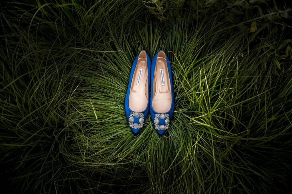 A pair of blue high-heeled shoes with embellishments, perfect for a Rhode Island wedding, placed on a bed of green grass.