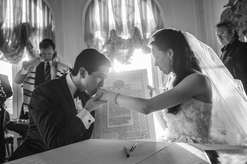 A groom kissing the hand of his bride during a Pine Hollow Country Club wedding ceremony with guests in the background.