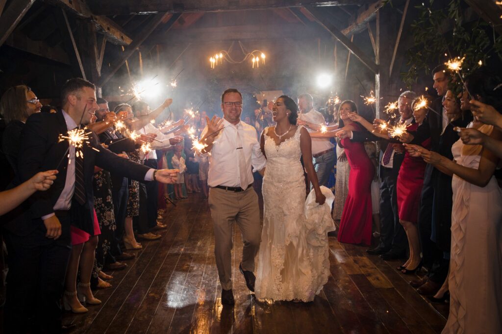 A bride and groom walk through a tunnel of guests holding sparklers at a nighttime Riverside Farm wedding reception.