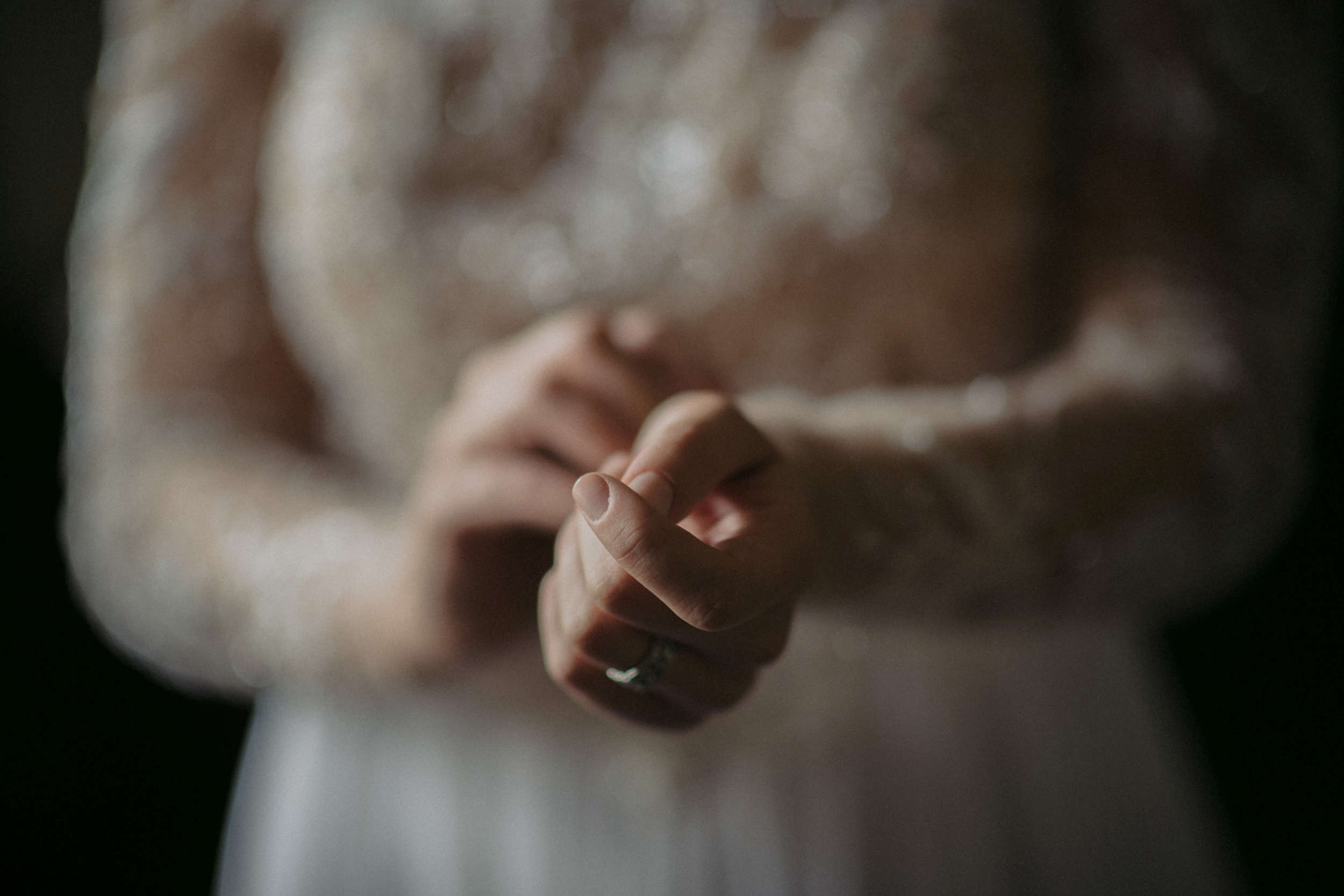 Close-up of a bride’s hands clasped together at a Hotel du Village wedding, showcasing a wedding ring, with focus on the ring and lacy sleeve details.