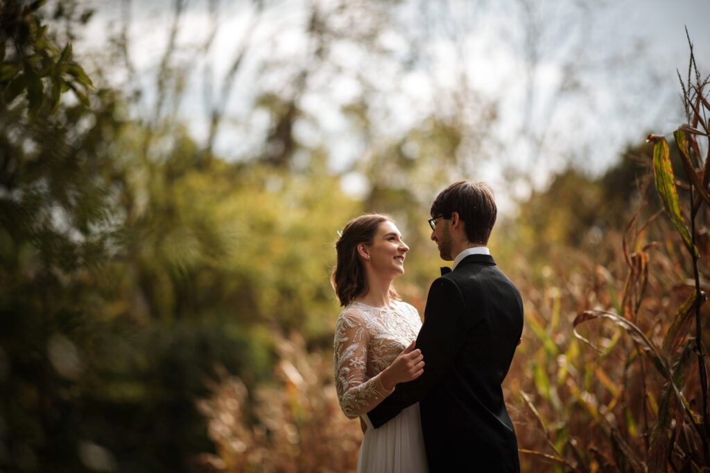 A bride and groom sharing a tender moment in a rustic field at their Hotel du Village wedding, surrounded by tall, golden foliage.