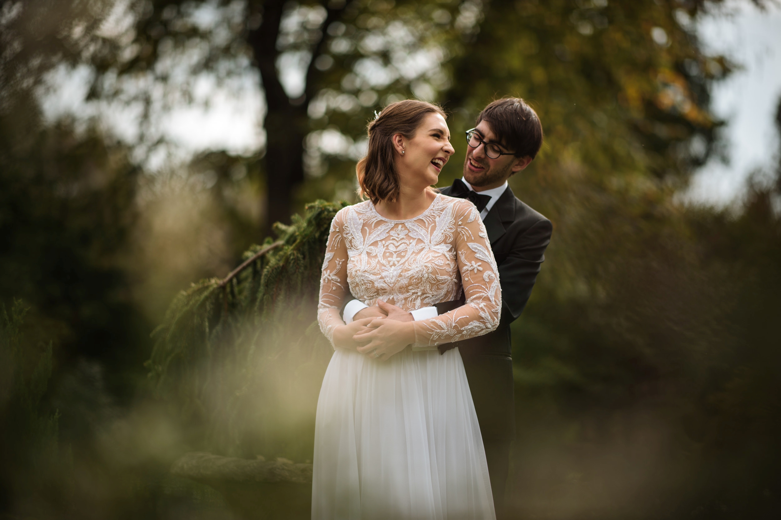 A bride and groom smiling and embracing in a sunlit garden at Hotel du Village, with the focus on the bride as she looks away joyfully.