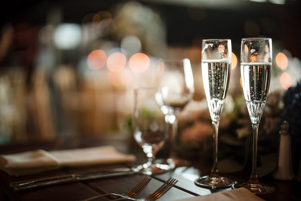 Two champagne flutes filled with sparkling wine on a dining table at a Saltwater Farms Vineyard wedding, with soft focus lights in the background.