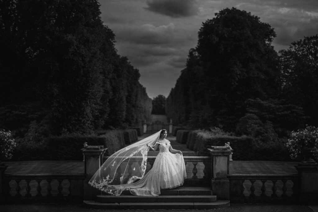 Bride standing alone on a staircase at Old Westbury Gardens, with her veil flowing in the wind.