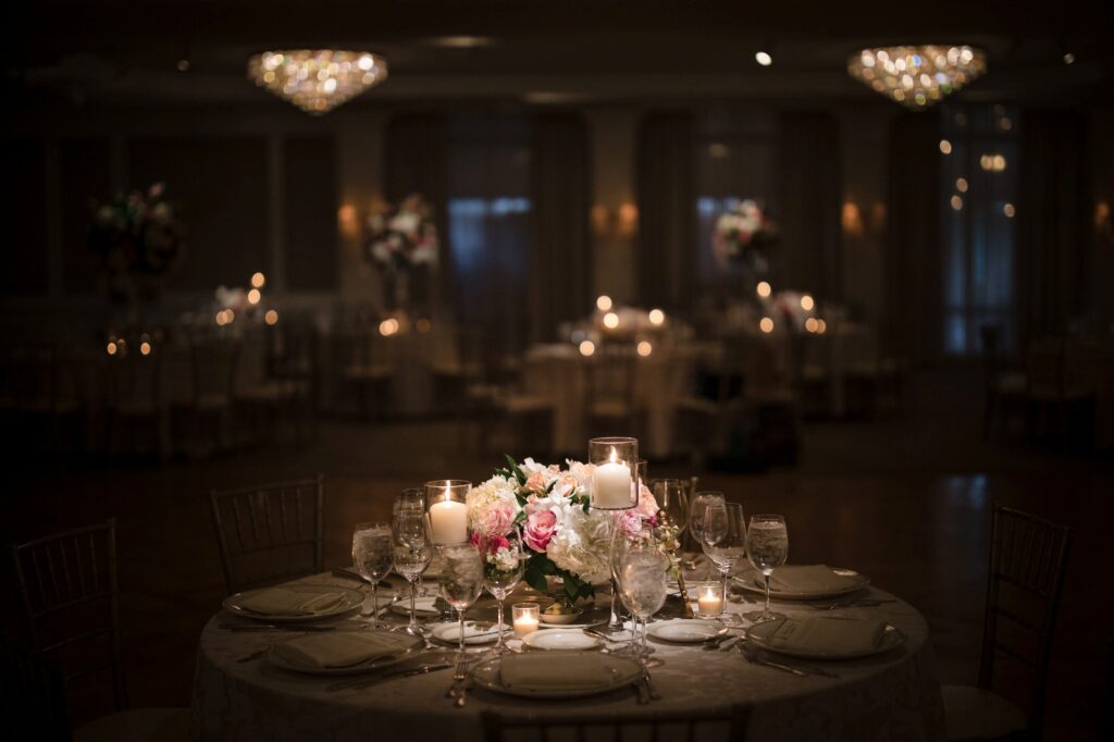 Elegant banquet table setting with floral centerpiece at a Pine Hollow Country Club wedding in a dimly lit room with chandeliers.