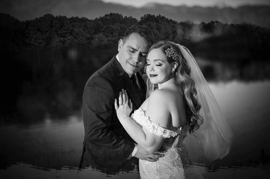 A black and white photo of a bride and groom embracing lovingly by the tranquil Rock Island Lake Club.