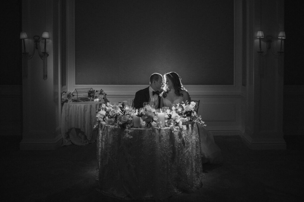 Bride and groom share an intimate moment at a dimly-lit pine hollow country club wedding reception table adorned with flowers.