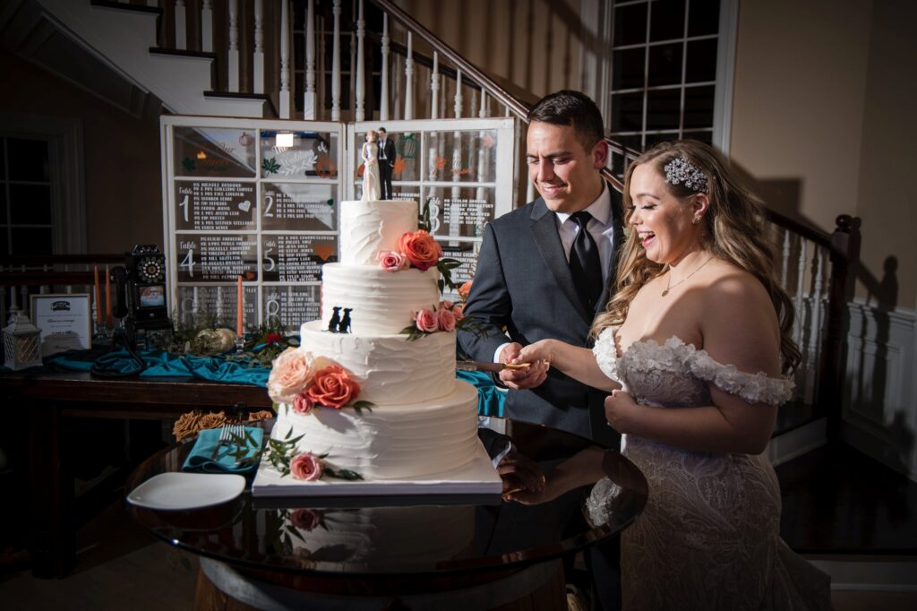 Bride and groom cutting a multi-tiered wedding cake with peach and white flowers at their Rock Island Lake Club wedding in an elegantly lit indoor setting.