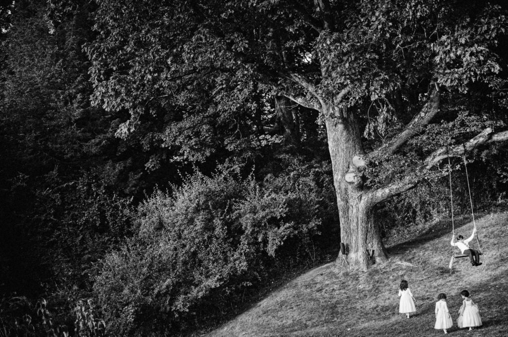 Children in white dresses playing near a tree with a swing in the shaded park area of Crossed Keys Inn, Andover.