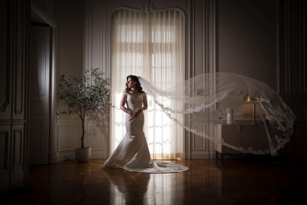 Bride in an elegant dress with a flowing veil illuminated by natural light in a classic room at Pine Hollow Country Club wedding.