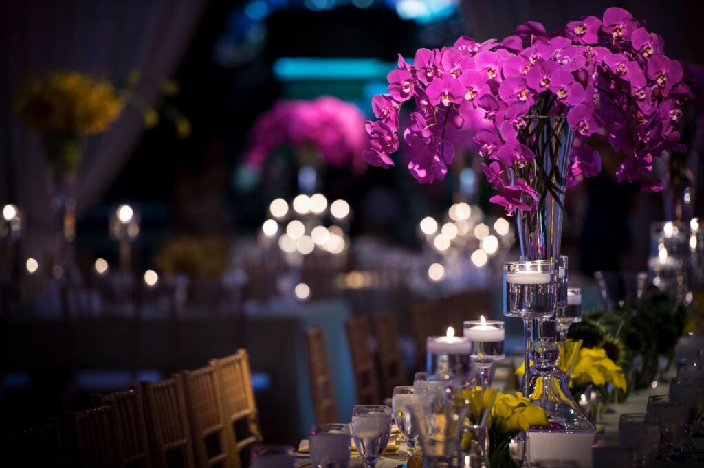 Elegant Please Touch Museum wedding reception table with a tall, crystal vase showcasing vibrant purple orchids, surrounded by lit candles and soft lighting.